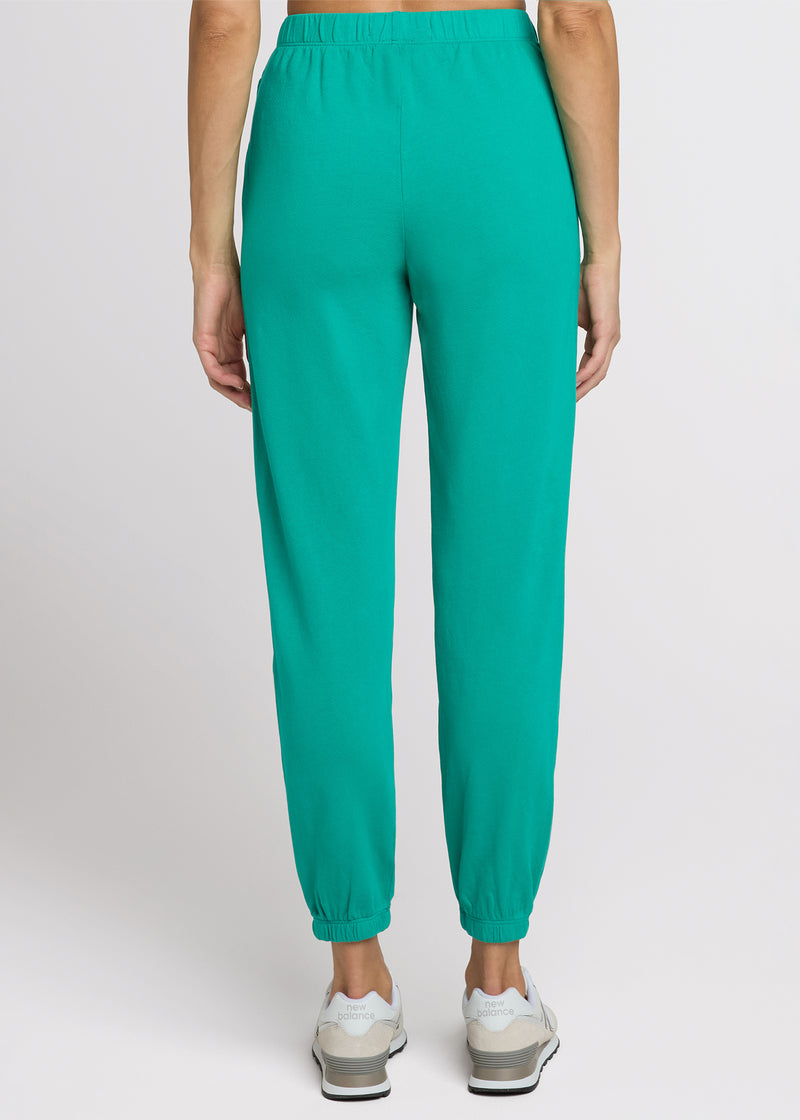 Woman in green sweatpant standing with her hands at her side. Back. 