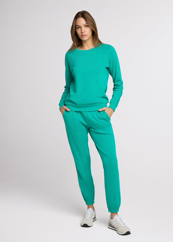 Woman in green sweatpant and green sweatshirt standing with her hands at her pockets.