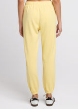 Woman in yellow sweatpant standing with her hands at her side. Back.