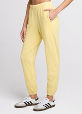 Woman in yellow sweatpant standing with her hands in her pockets. Side.