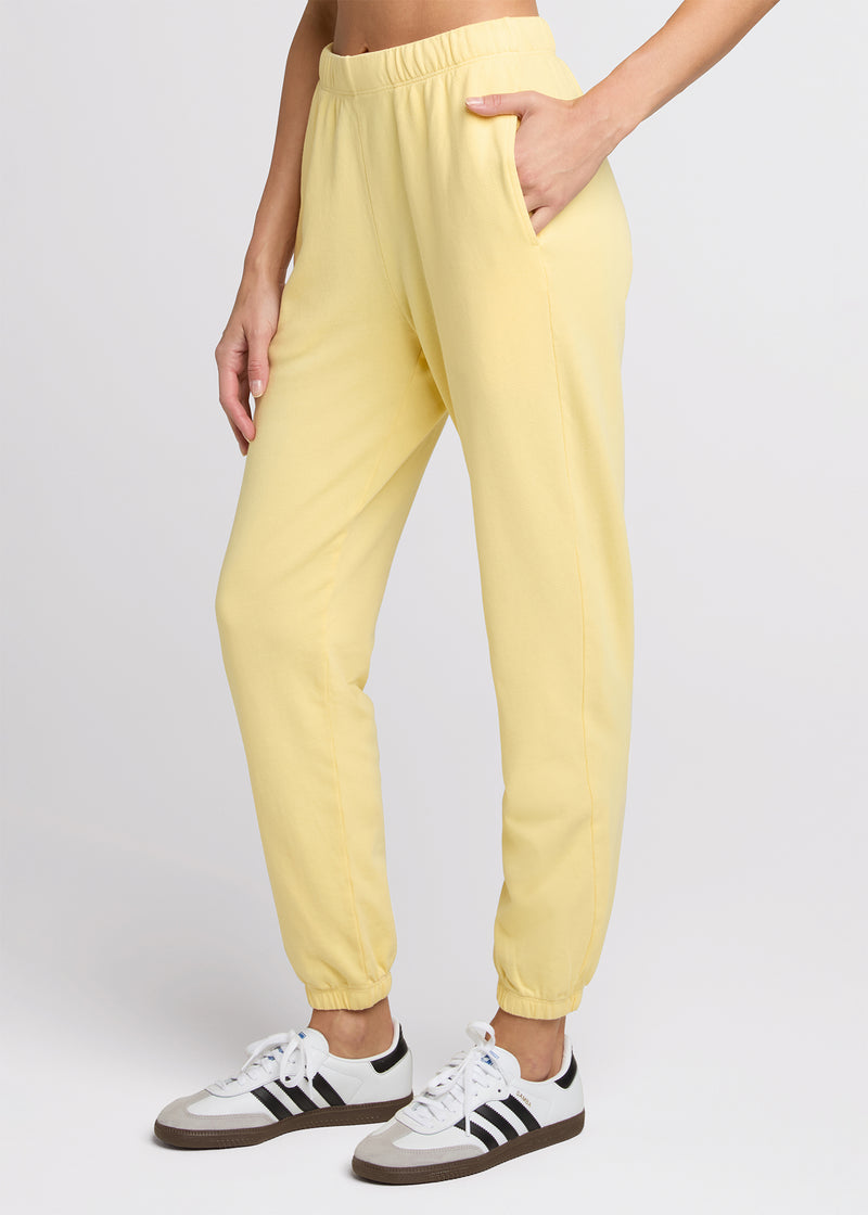 Woman in yellow sweatpant standing with her hands in her pockets. Side.