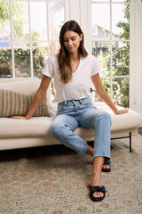 Woman in white v neck tee and blue denim sitting on a couch inside an elegant living room while looking at the ground. 