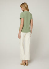 Woman in v neck t-shirt and cream cropped denim with nude wedges and her hands at her side. Back.