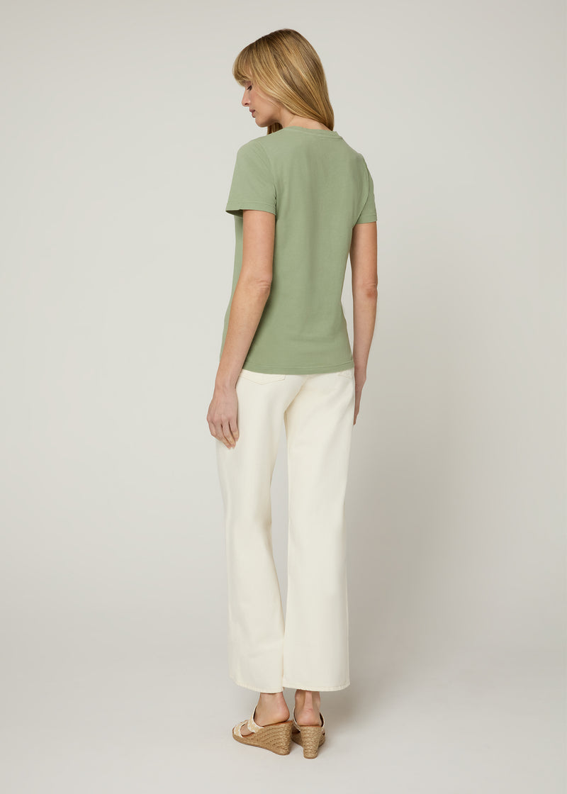 Woman in v neck t-shirt and cream cropped denim with nude wedges and her hands at her side. Back.