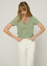 Woman wearing green v neck t-shirt tucked in cream colored jeans with her hands in her front pockets as she looks at the ground. Close up.