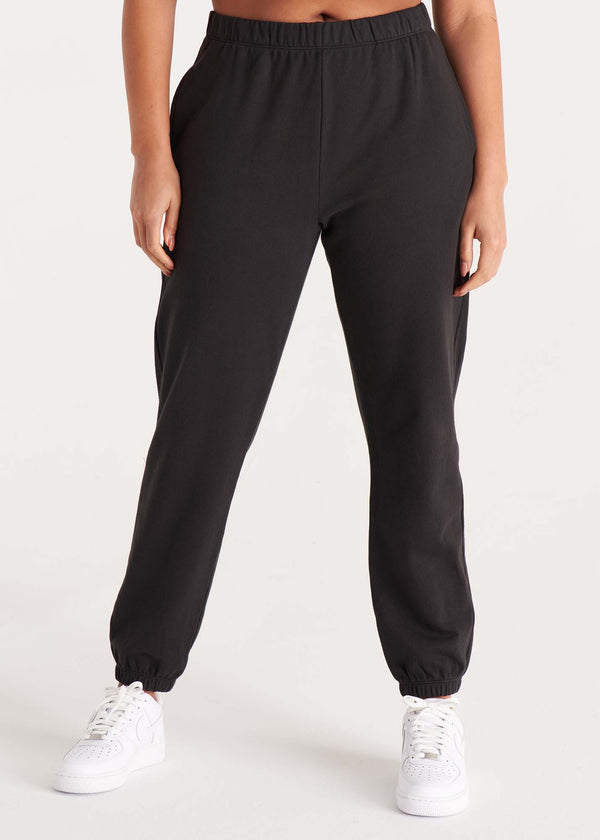 Woman in high-rise, relaxed fit sweatpant with an elastic waist, side pockets, and interior drawstring made of organic and recycled cotton French Terry and eco-friendly dyes in color onyx black, front image.