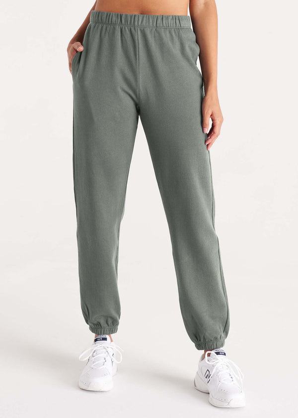 Woman in high-rise, relaxed fit sweatpant with an elastic waist, side pockets, and interior drawstring made of organic and recycled cotton French Terry and eco-friendly dyes in color thyme green, front