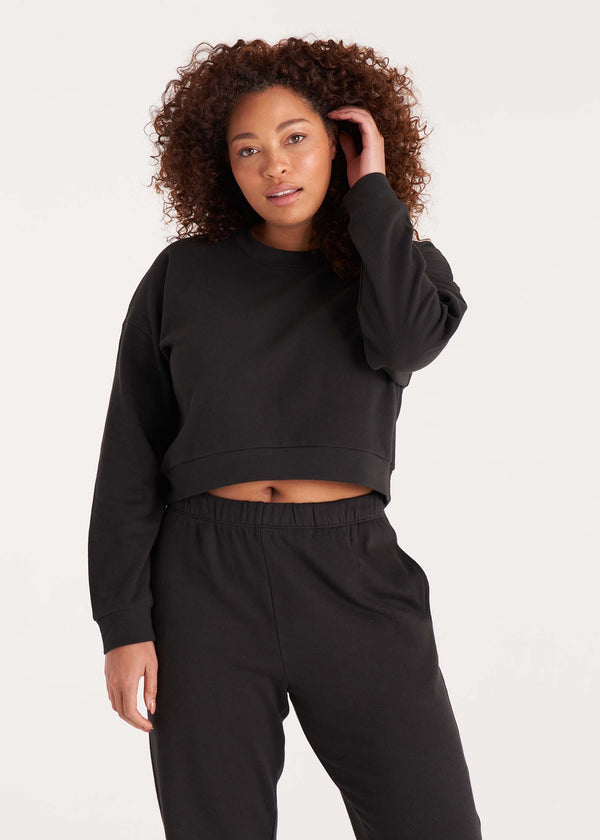 Woman in crewneck cropped sweatshirt with drop shoulders and length to midriff made of organic and recycled cotton French Terry in color Onyx Black, front