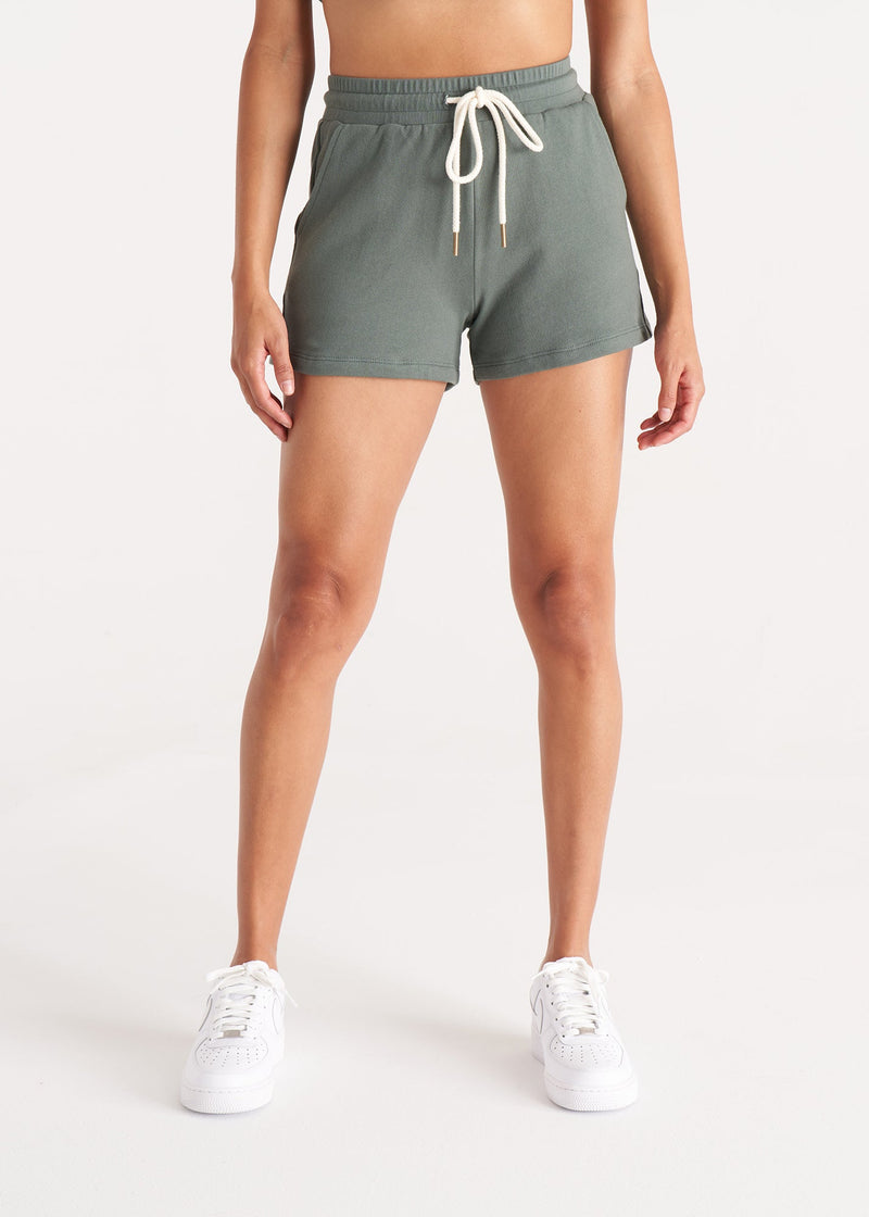Woman in relaxed fit jogger shorts made of organic and recycled cotton French Terry with elastic waist, side pockets, and brass capped drawcords in color Thyme Green, Detail