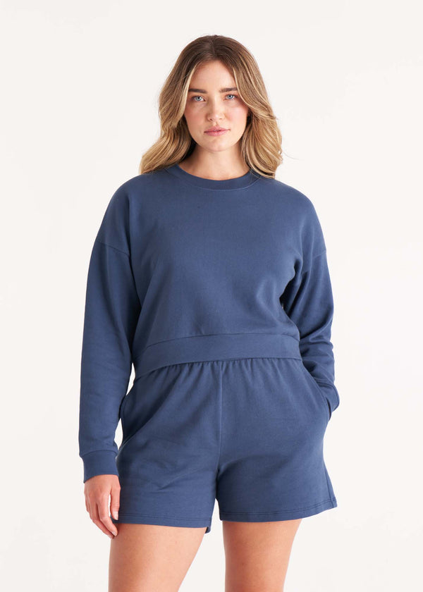 Woman in crewneck cropped sweatshirt with drop shoulders and length to midriff made of organic and recycled cotton French Terry in color Midnight Navy paired with a cropped sweatshirt