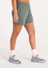 Woman in relaxed fit sweat shorts with elastic waist, side pockets, and interior drawcords made of organic and recycled cotton French Terry in color Thyme Green, Side