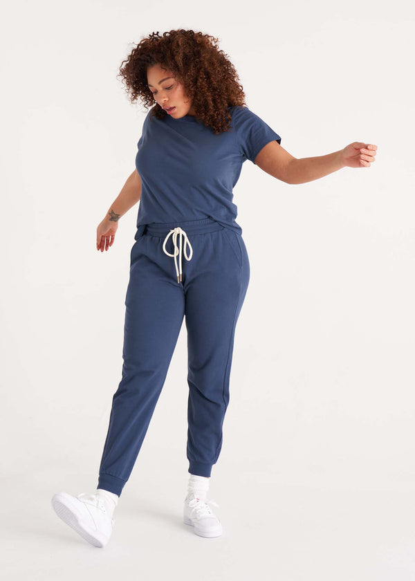 Woman in relaxed fit, mid-rise jogger pant with an elastic waist, pockets at sides, and brass capped drawcords in organic and recycled cotton French Terry in color midnight navy paired with a crew neck tee